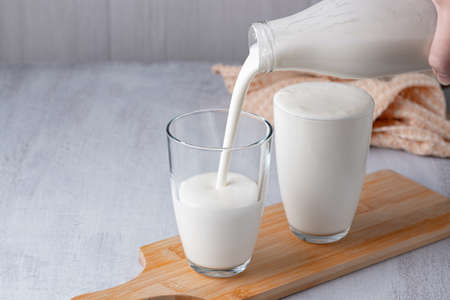 Pouring homemade kefir, buttermilk or yogurt with probiotics. Yogurt flowing from glass bottle on light background. Probiotic cold fermented dairy drink. Trendy food and drink. Copy spaceの写真素材
