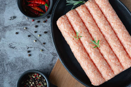 Raw homemade sausages (chicken, turkey) in a pan on a dark background with spicesの写真素材