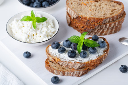Home made bread on a wooden cutting board with curd cheese and blueberries and mintの写真素材