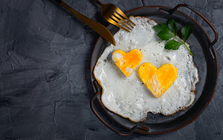Homemade fried egg in a vintage pan a grey background. Heart-shaped yolk.View from above. Copy space for textの写真素材
