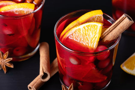 Mulled wine in glass glasses with spices and citrus fruits on a black wooden tableの写真素材