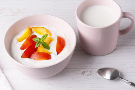 Fresh cottage cheese in pink bowl with mint leaves and peach pieces and milk on white backgroundの写真素材