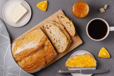 Cup of coffee, sandwich with orange jam, loaf of bread on the gray background. Breakfast concept.