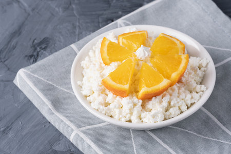Fresh cottage cheese in white bowl with orange pieces on white background. Copy spaceの写真素材