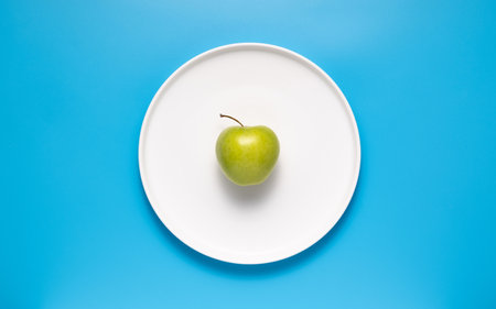 Fresh green apple on a white plate on a blue backgroundの写真素材