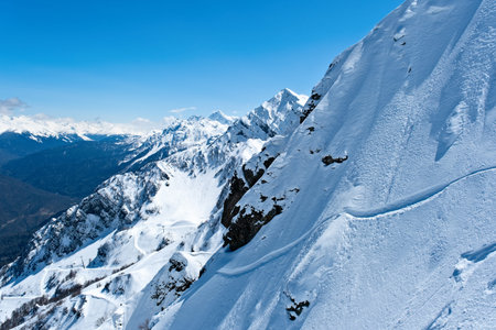 Snow-covered mountain range under a clear blue sky with distant peaks in the afternoon