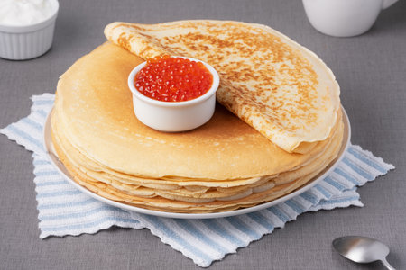 Delicious stack of golden pancakes served with cream and caviar on a rustic tableの写真素材