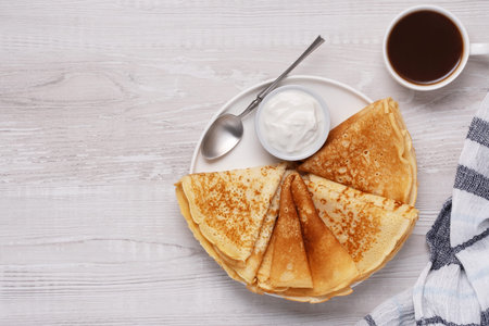 Breakfast with pancakes, cream, and coffee on a wooden table during the morning.