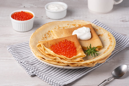 Delicious crepes topped with red caviar served on a cozy table setting in daylight
