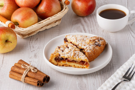 Delicious apple pie slices served with coffee, apples and cinnamon sticks on a rustic wooden table during a cozy afternoonの写真素材