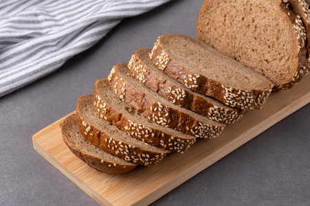 Freshly sliced whole grain bread with sesame seeds on a wooden cutting board