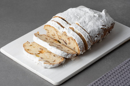 Delicious sliced traditional stollen bread with nuts and powdered sugar resting on a wooden board