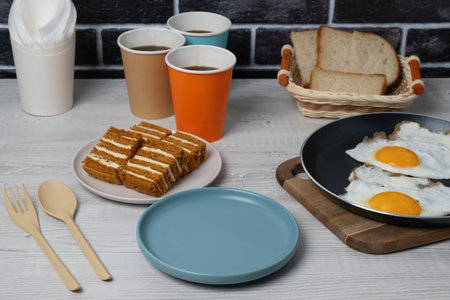 Breakfast setup with eggs, cake, coffee, and bread on a wooden table in a cozy kitchen