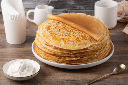 Stack of golden crepes served with sour cream on a wooden tableの写真素材