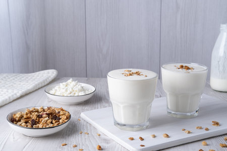 Kefir, buttermilk or yogurt, cottage cheese with granola. Yogurt in glass on white wooden background. Probiotic cold fermented dairy drink. Gut health, fermented products, healthy gut flora conceptの写真素材