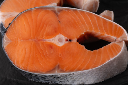 A salmon fillet is cut in half, revealing bright orange flesh. The surface is smooth and clean, showing the layers of the fish. The fillet is on a dark surface.の写真素材