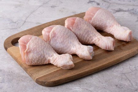 Four raw chicken drumsticks are placed neatly on a wooden cutting board. They are ready to be seasoned and cooked for a meal at home.の写真素材