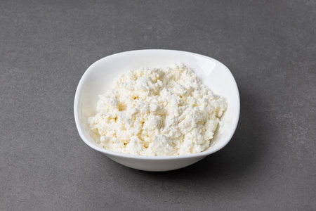 Cottage cheese in a white bowl on a gray surface in a kitchen setting showing fresh dairy food ready to serveの写真素材