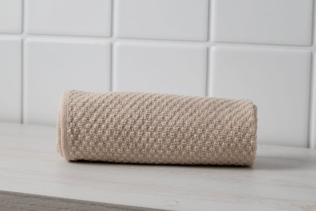 Towel is neatly rolled on a wooden shelf near white tiled wall in a bathroom settingの写真素材