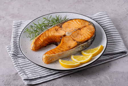 Seared salmon steak with rosemary and lemon pieces on grey tableの写真素材
