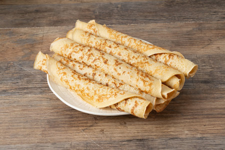 Stack of thin crepes on a white plate placed on a wooden tableの写真素材