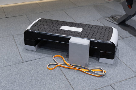 A step platform is set up on a gray gym floor alongside a foam block and resistance bandsの写真素材