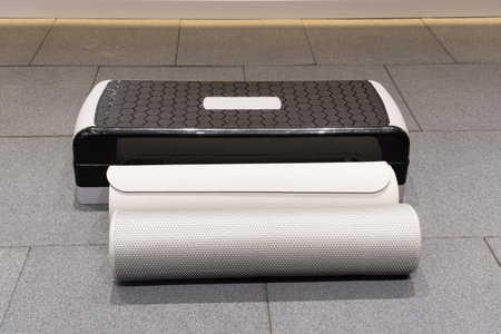 Fitness tools are arranged on a smooth gray floor. There is a step platform and two exercise mats.の写真素材