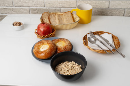 Breakfast spread with bread, bagels, oats, and fruit on a simple kitchen table in a bright roomの写真素材