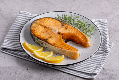 Seared salmon steak with rosemary and lemon pieces on grey tableの写真素材
