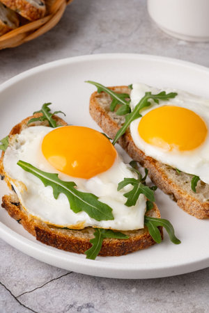 Breakfast with eggs on toast and fresh arugula served on a white plate in a kitchen setting