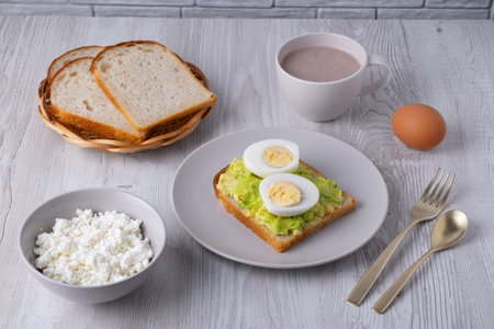 Healthy breakfast with toast, boiled eggs, cottage cheese, bread, and hot drink served on a wooden...