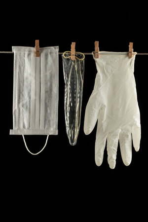white plastic gloves, mask, condom hanging on the rope with wooden pegs on a black background close-upの写真素材