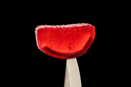 close-up of colorful soft candy on the tip of a metal knife on a black backgroundの写真素材