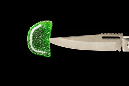close-up of colorful soft candy on the tip of a metal knife on a black background