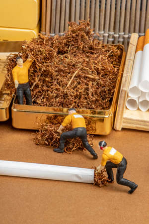 close-up studio concept of factory producing and shipping cigarettes from unhealthy product tobacco with miniature worker boss human figuresの写真素材