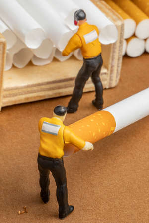 close-up studio concept of factory producing and shipping cigarettes from unhealthy product tobacco with miniature worker boss human figuresの写真素材