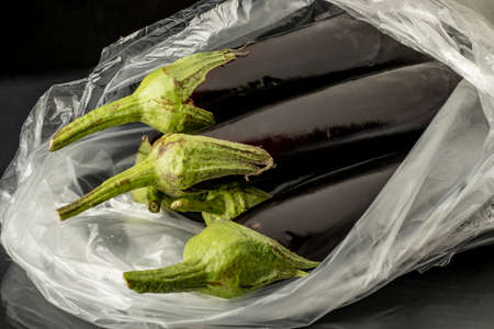 close-up fresh purple eggplant in transparent bag on black backgroundの写真素材