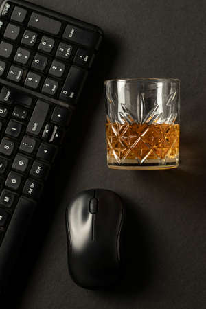 close-up black background vertical computer keyboard and mouse, desktop concept with glass of whiskey parallel to horizontal gravityの写真素材
