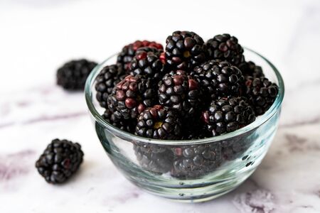 Fresh blackberries in a clear glass bowl isolated on marble table backgroundの写真素材