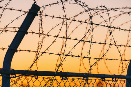 Barbed wire fence on sunset background. Selective focus. Shallow depth of fieldの写真素材