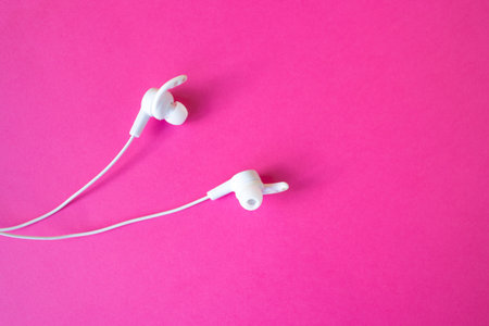 White headphones with a wire on a pinkbackground. The concept of gadgets.