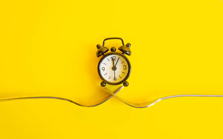 Black clock on a yellow background. Alarm clock on two forks, trend concept time .の写真素材