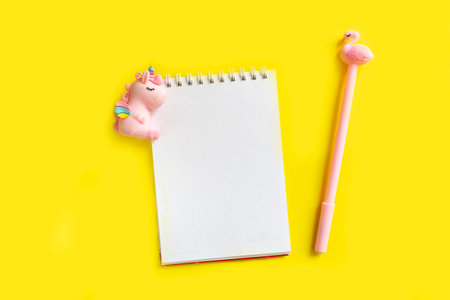 Blank white notepad on a spiral with a pink pen. Top view with copy space, flat lay on yellow...