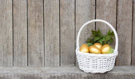 Easter, golden eggs in a white basket. Wooden background with copy space.