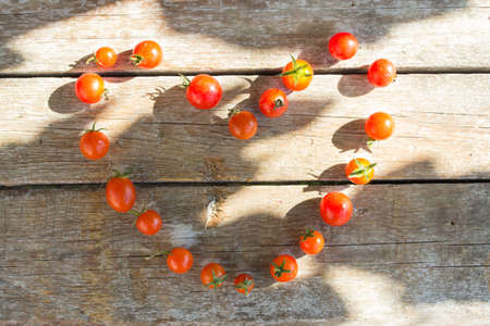 Small cherry tomato, tomatoes on a wooden background lined in the shape of a heartの写真素材