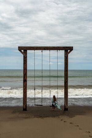 Lonely woman on a swing at a beachの写真素材