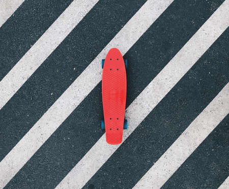 Red cruiser board on dark gray and white crosswalk. Plastic penny skateboard on asphalt, shot from the top.の写真素材