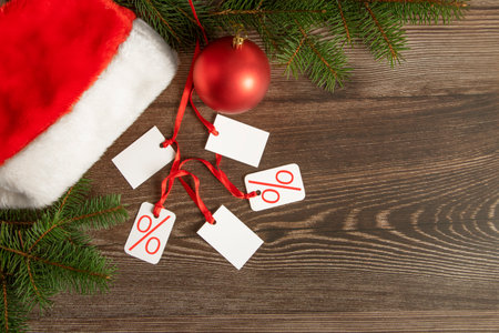 Christmas shopping. Santa hat, red Christmas ornament and white discount tags on dark wooden background top viewの写真素材
