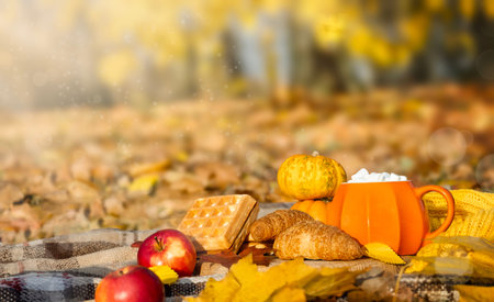 Autumn picnic in the park. Orange cup of coffee with marshmallow, apple and croissants and waffles on picnic blanket on nature yellow leaves. Active lifestyle conceptの写真素材