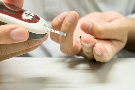 Medicine, diabetes, glycemia, health care and people concept - close up of man hands checking blood sugar level by Glucose meterの写真素材